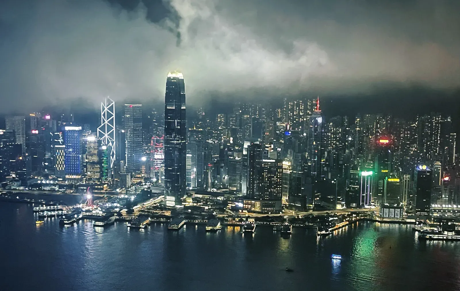 Lit high-rise skyline across dark water under low night cloud.