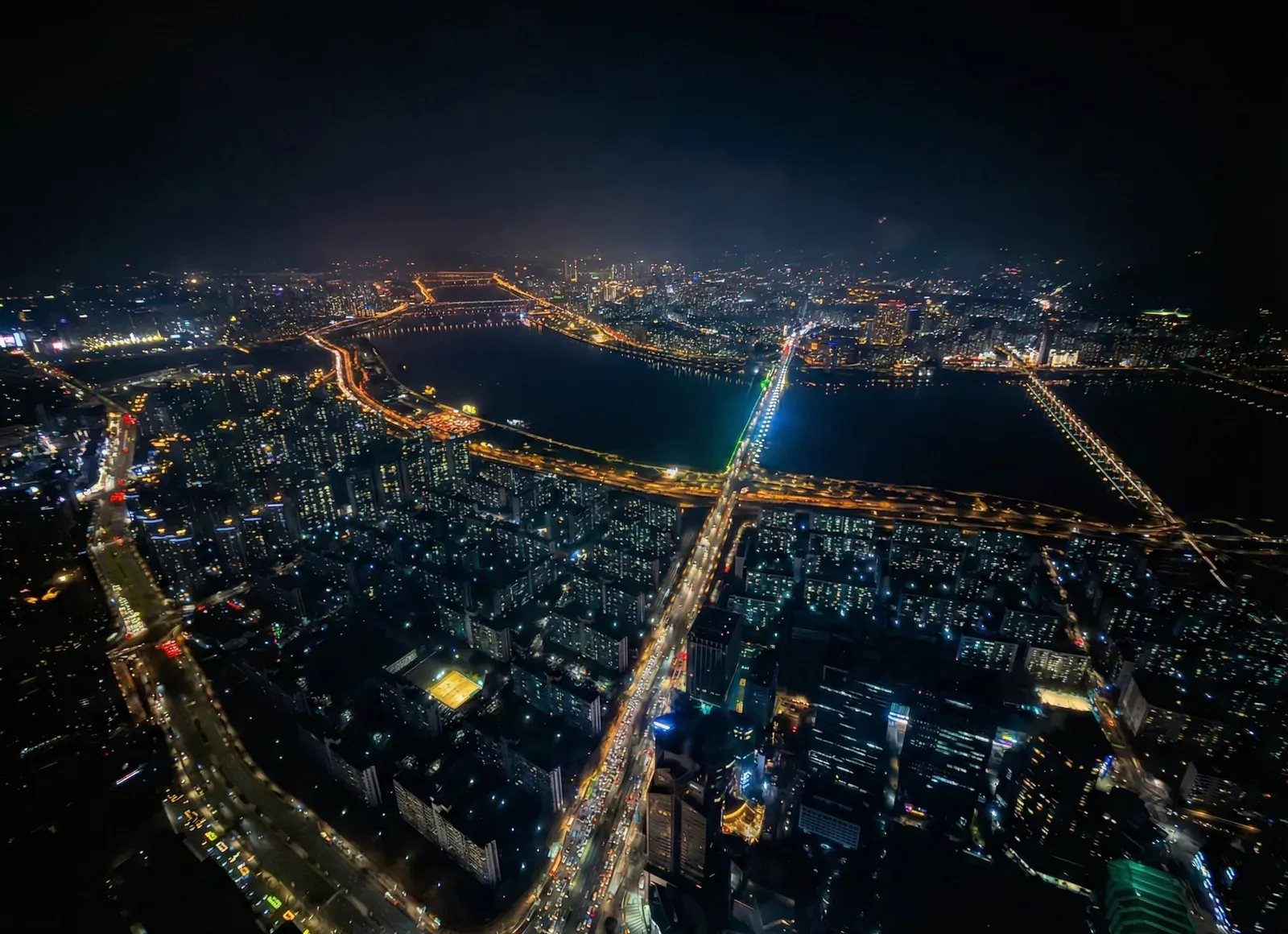 Night city from above, a wide river crossed by lit bridges.