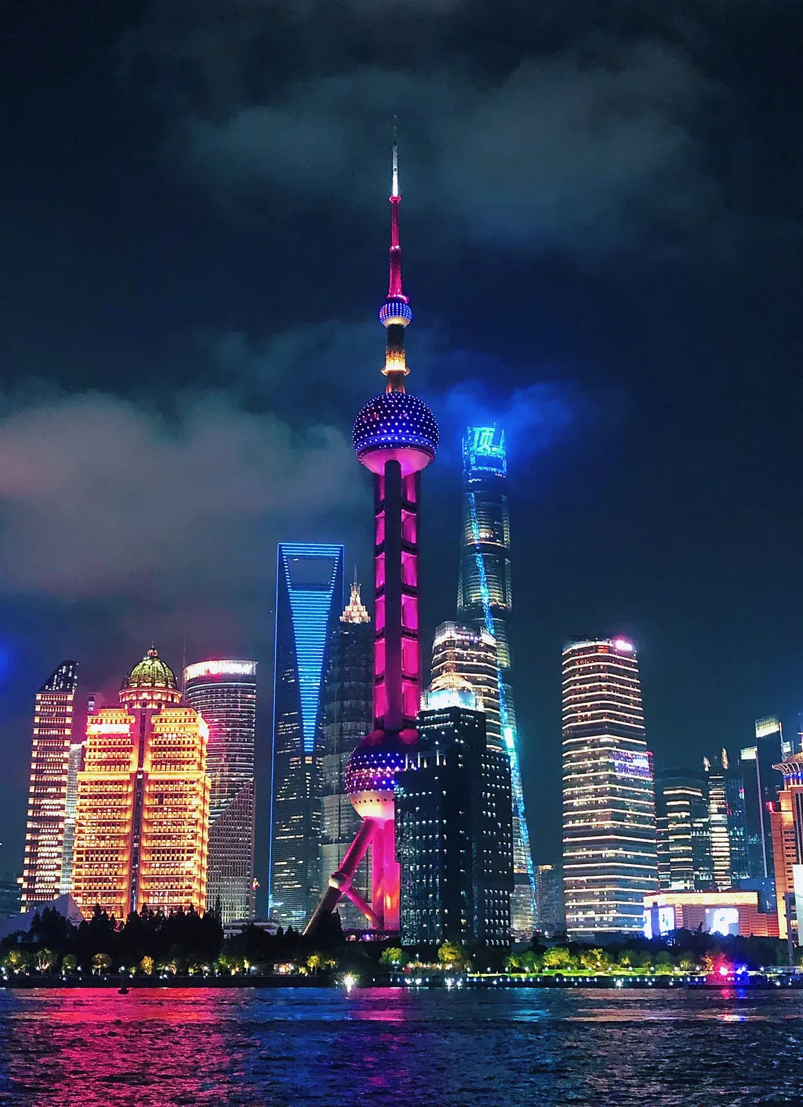 Neon-lit riverside towers under heavy night cloud.