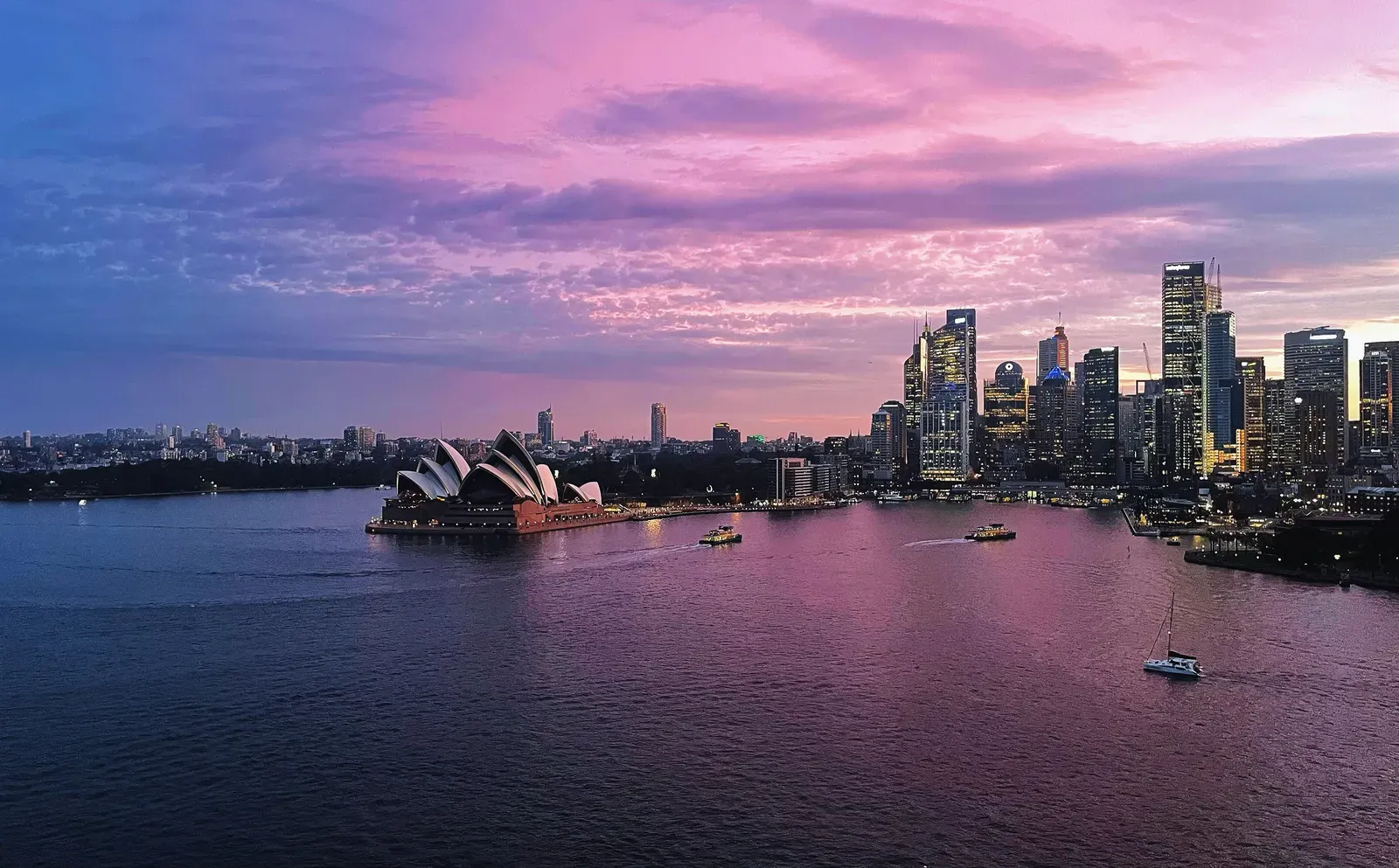 Harbour at pink dusk, ferries crossing toward a lit downtown.