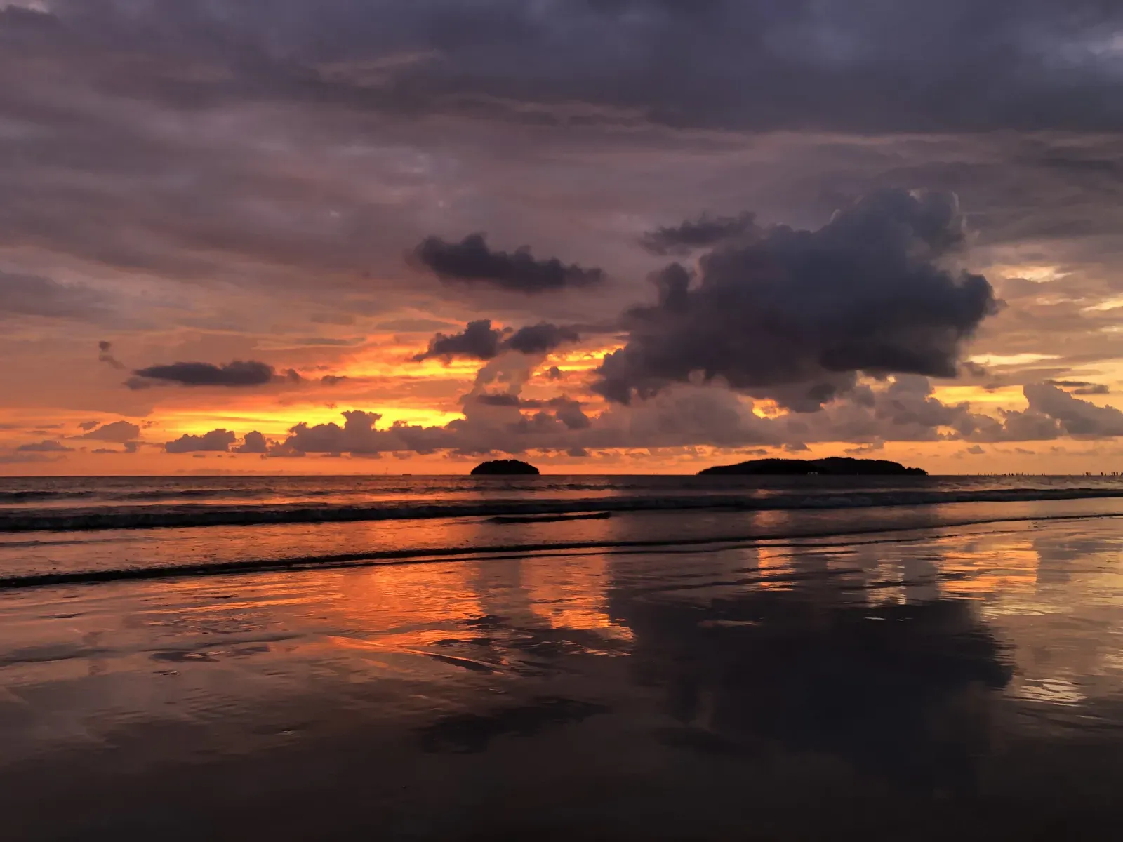 Two small islands beyond a wet beach at cloudy sunset.