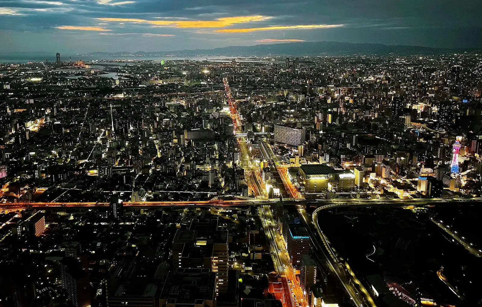 Night city stretching to the sea under an orange horizon.