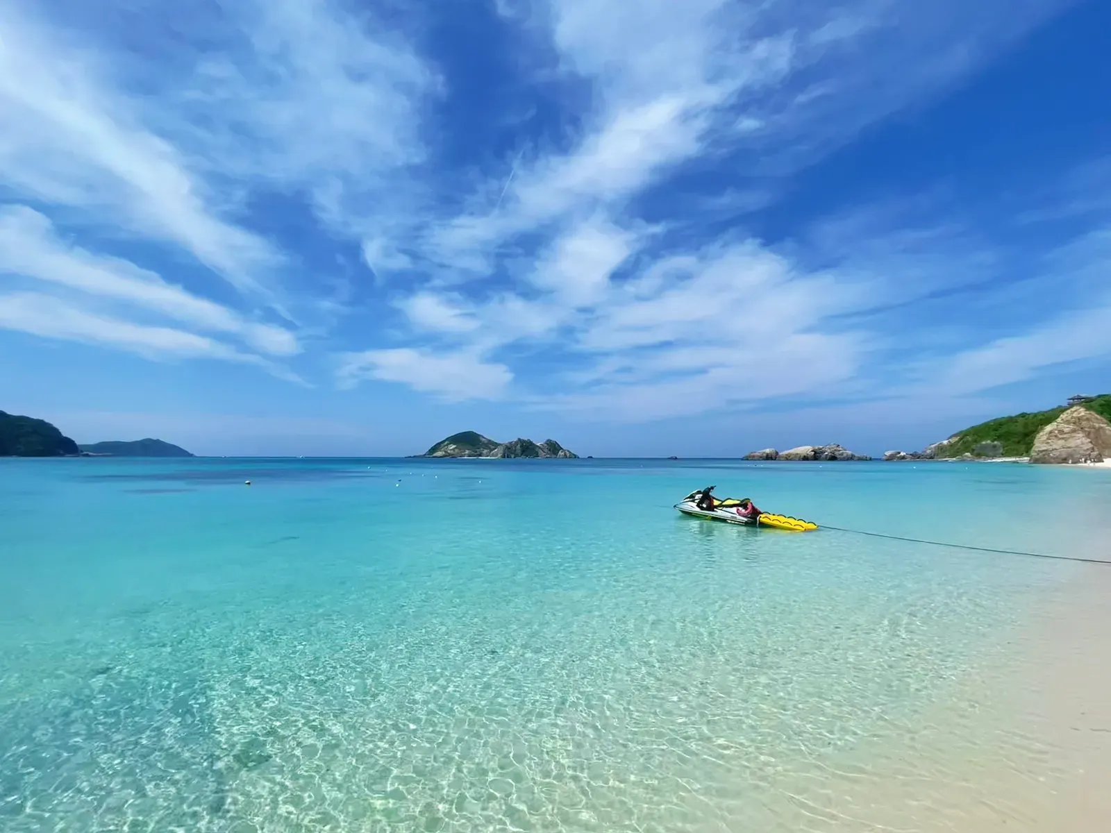 Clear turquoise shallows and a moored jet ski off white sand.