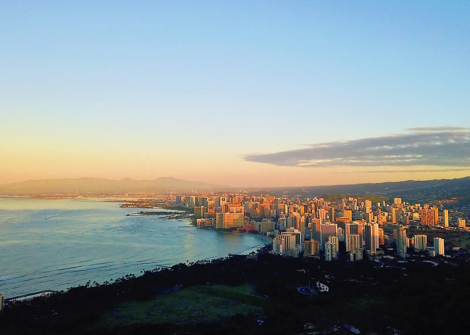 Coastal city catching first sun, seen from a high ridge.