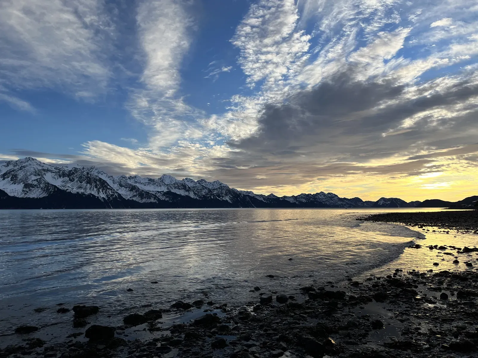 Snow peaks across a bay under a broad cirrus sky.
